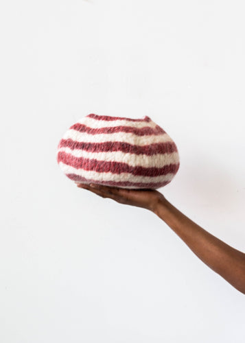 Hand holding a red and white striped wool bowl against a white background