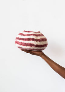 Hand holding a red and white striped wool bowl against a white background