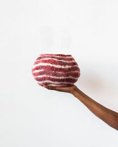 Hand holding a red and white striped wool basket against a white background