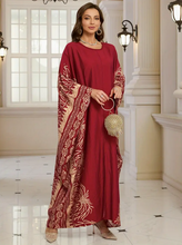 Woman in a red dress with gold patterns standing in an elegant interior setting.