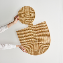 Woven rattan wall art piece held by a person against a white background