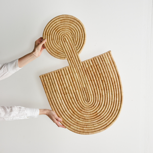 Woven rattan wall art piece held by a person against a white background