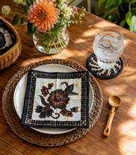 Table setting with floral napkin, glass of water, and wooden spoon on a wooden table.