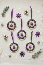 Decorative Christmas ornaments with purple ribbons and snowflake decorations on a textured white background.