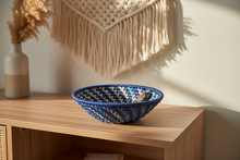 Blue woven basket on a wooden surface with a decorative wall hanging in the background