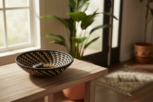 Woven basket on a wooden table with plants and a window in the background