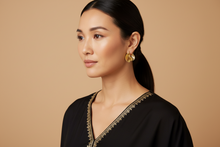 Woman wearing a black saree with gold trim against a beige background