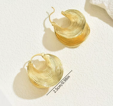 Gold hoop earrings on a textured white surface with measurement label.