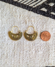Gold hoop earrings on a textured fabric surface with a penny for scale.