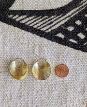 Gold hoop earrings next to a penny on a textured fabric background