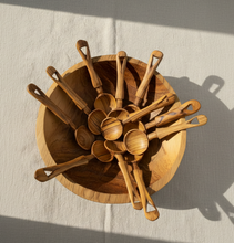 Wooden kitchen utensils including spoons and ladles in a wooden bowl on a light background