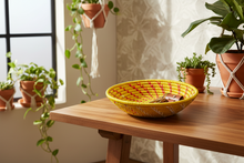Yellow woven basket on a wooden table with plants in the background