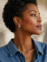 Woman wearing a blue shirt and smal silver hoop earrings with a neutral background
