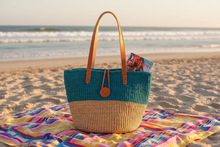 Woven bag on a colorful towel at the beach with ocean in the background