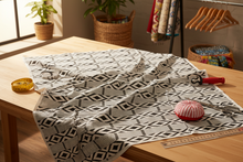 Fabric with an African geometric pattern on a wooden table, surrounded by sewing tools and materials.