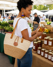 Woman at an outdoor market examining jars of honey with woven bag on her shoulder