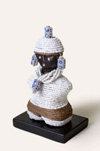 Decorative african art sculpture with white beadwork and brown rope on a black base against a white background