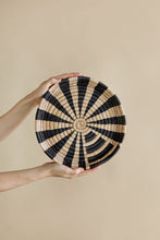 Woven black and beige circular wall art held by a person against a beige background