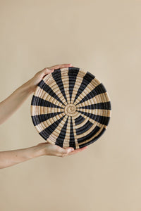 Woven black and beige circular wall art held by a person against a beige background