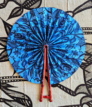 Blue paper fan with black patterns on a textured beige background