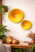 Yellow woven baskets on a wall with a wooden shelf below containing decorative items.