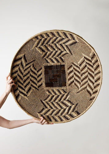 Woven basket with geometric pattern held by a person against a plain background